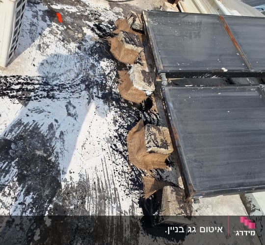חומר איטום שחור נמרח על גג ליד קולטים